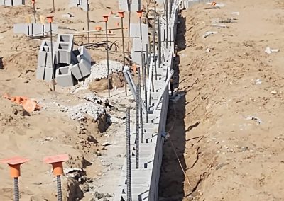 Concrete blocks and rebar forming a foundation at a construction site, with workers and vehicles in the background.