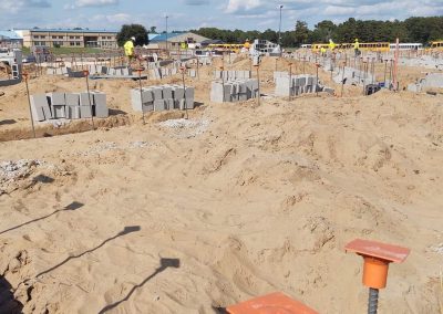 Construction site with sand, cinder blocks, rebar, and workers under a sunny, partly cloudy sky.