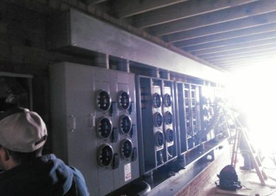 A row of electrical meter boxes is installed along a brick wall inside a building under construction.